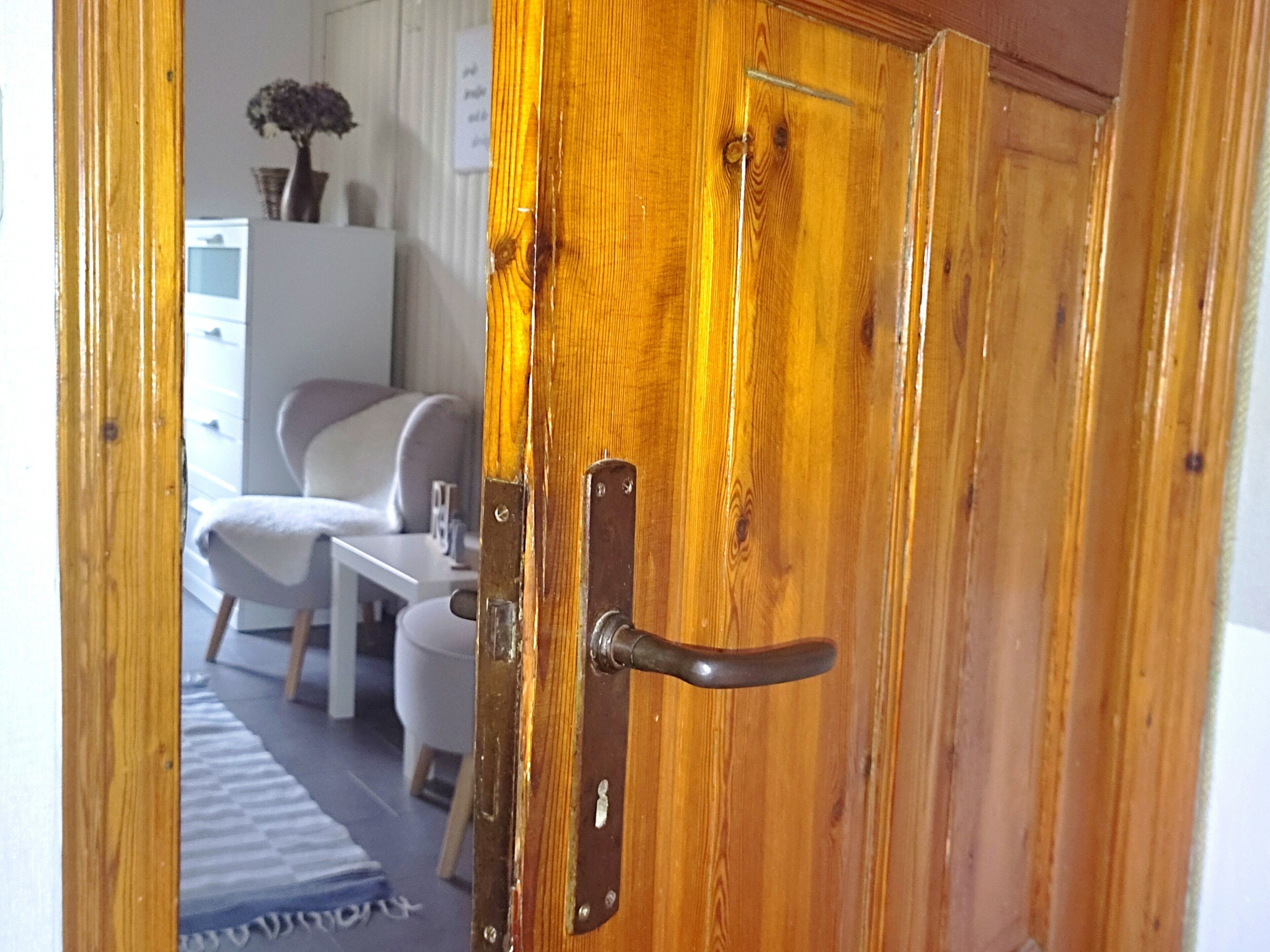 Une porte en bois avec une poignée en métal, une chaise blanche, une petite table et une plante en arrière-plan.