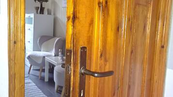 Une porte en bois avec une poignée en métal, une chaise blanche, une petite table et une plante en arrière-plan.