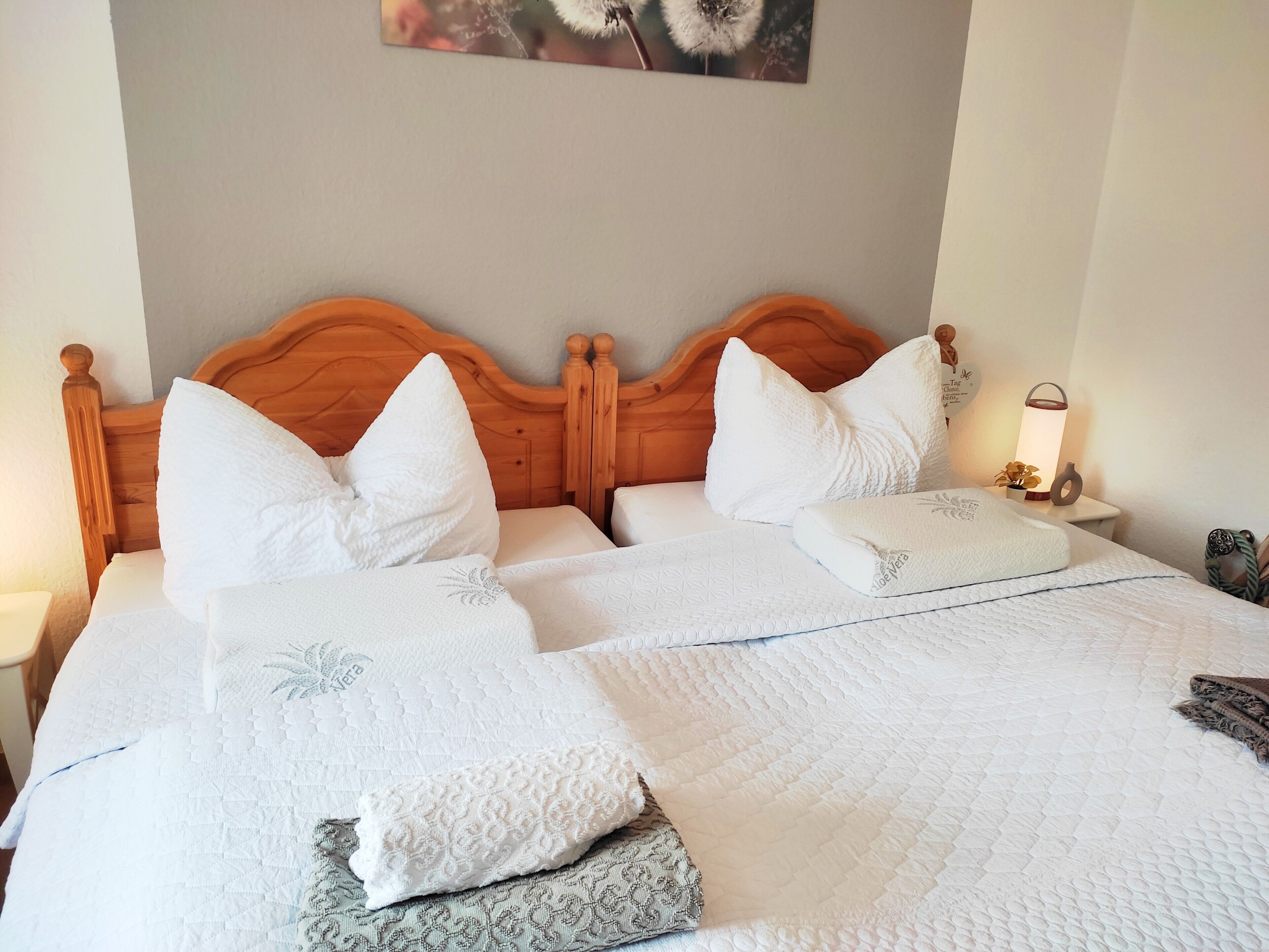 A double bed with a wooden headboard, white bedding, and a wall-mounted picture.