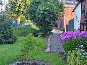 Un jardin résidentiel agrémenté d’un chemin pavé, d’un banc et de diverses plantes et fleurs.