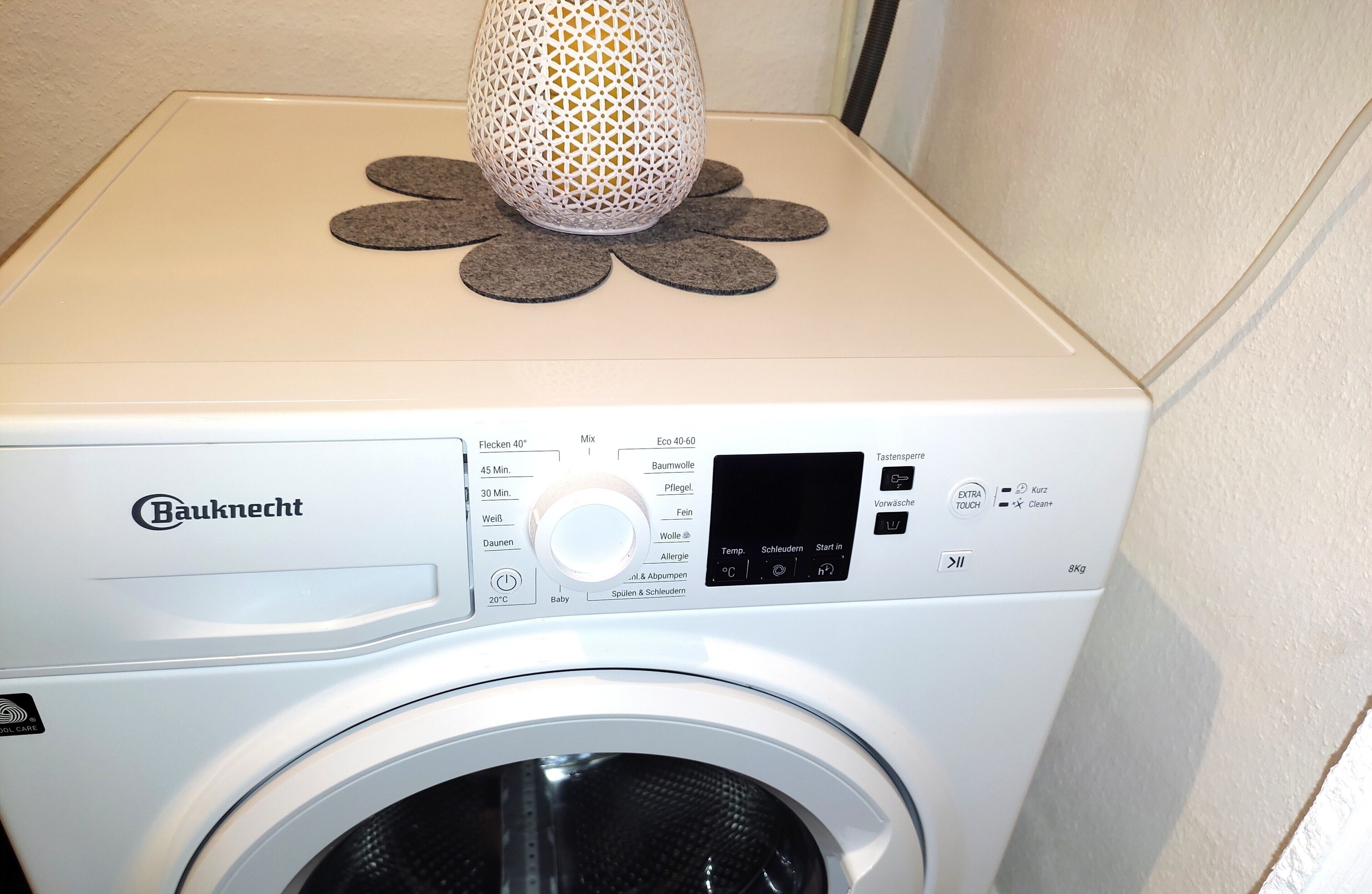 A Bauknecht washing machine with a control panel, a decorative item on top, and a white wall in the background.