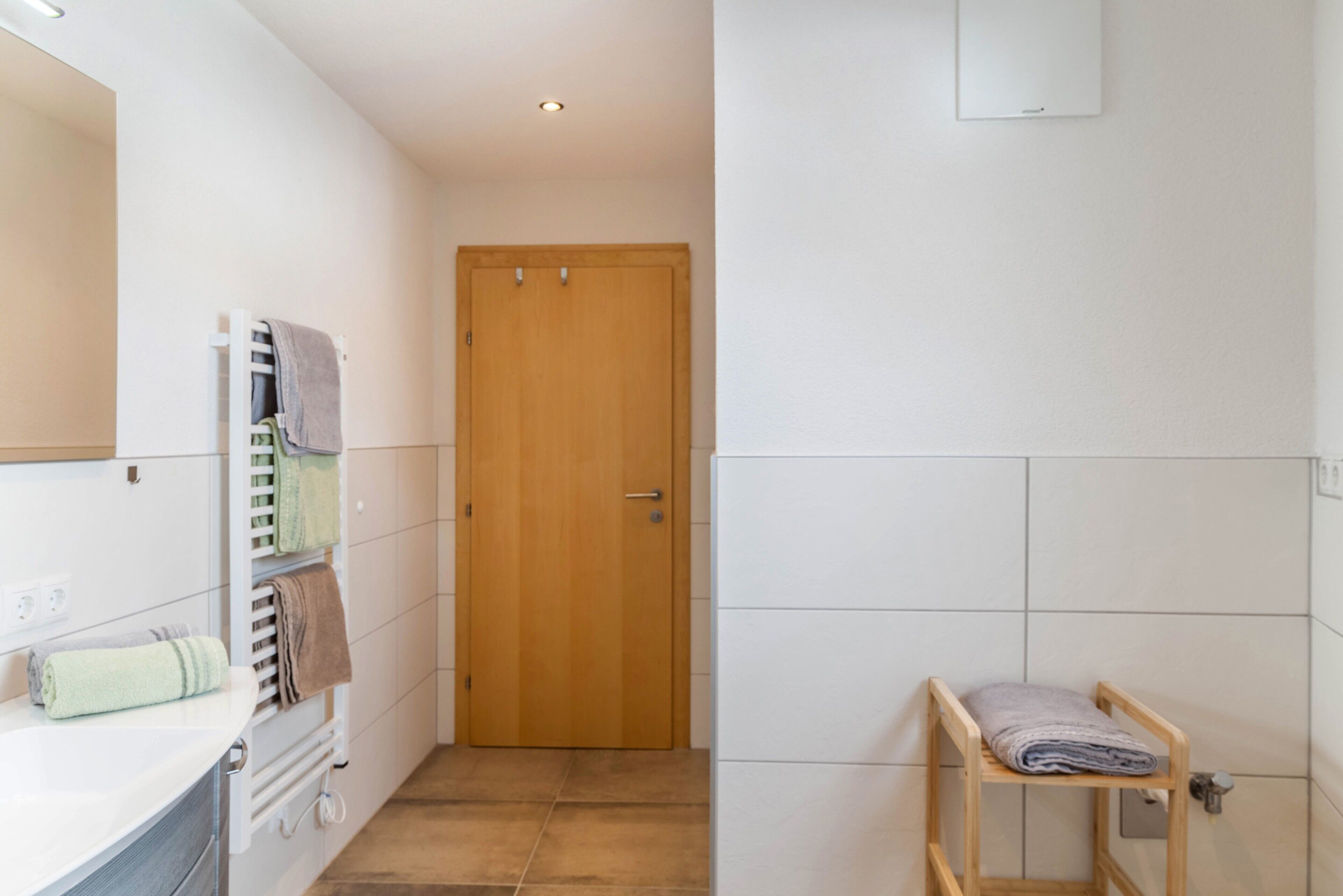 A bathroom with a wooden door, a towel rack with towels, and a small wooden shelf with a towel.