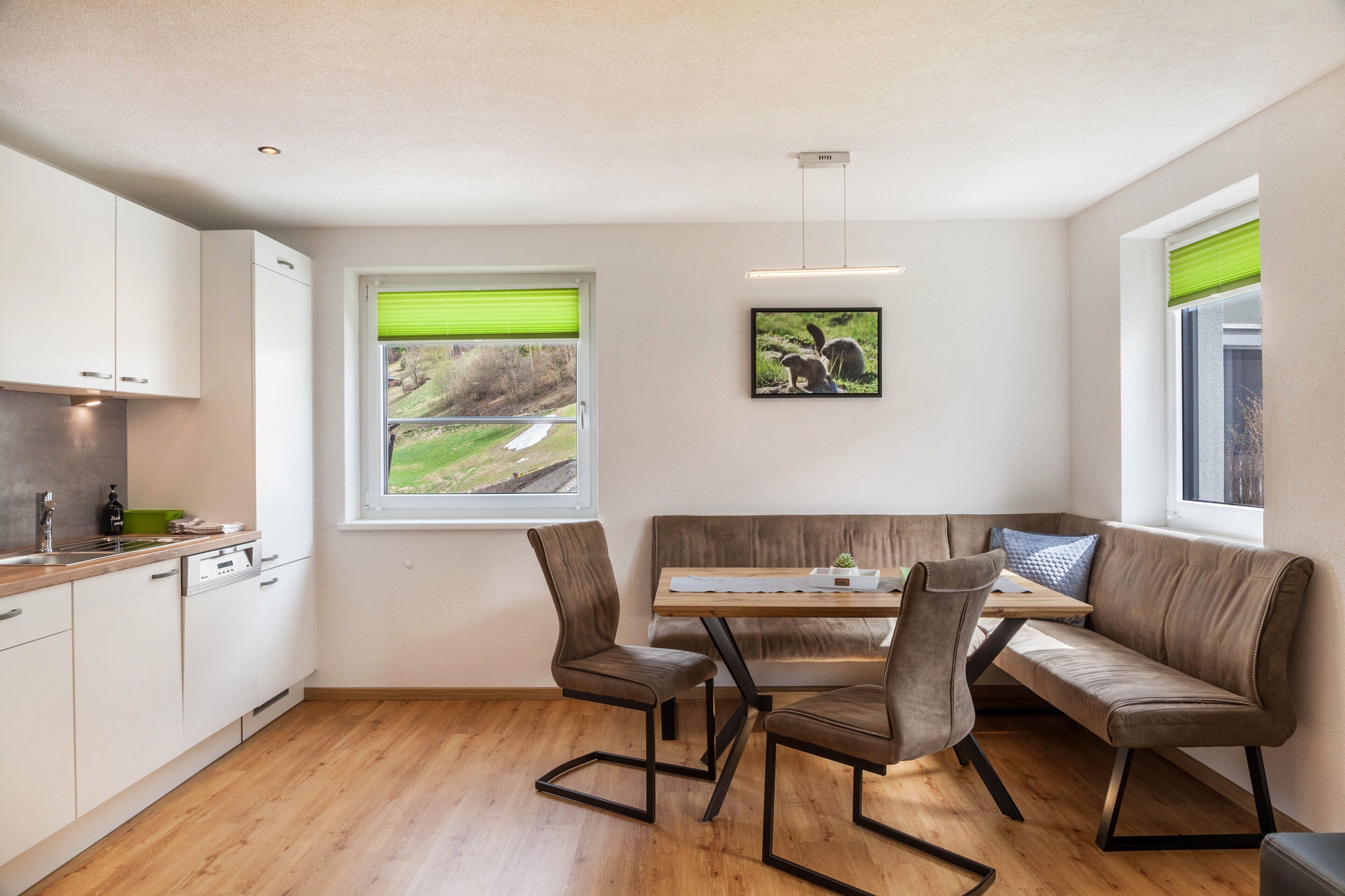 Une cuisine moderne avec des meubles blancs, un plan de travail en bois et un coin repas comprenant un banc et des chaises.