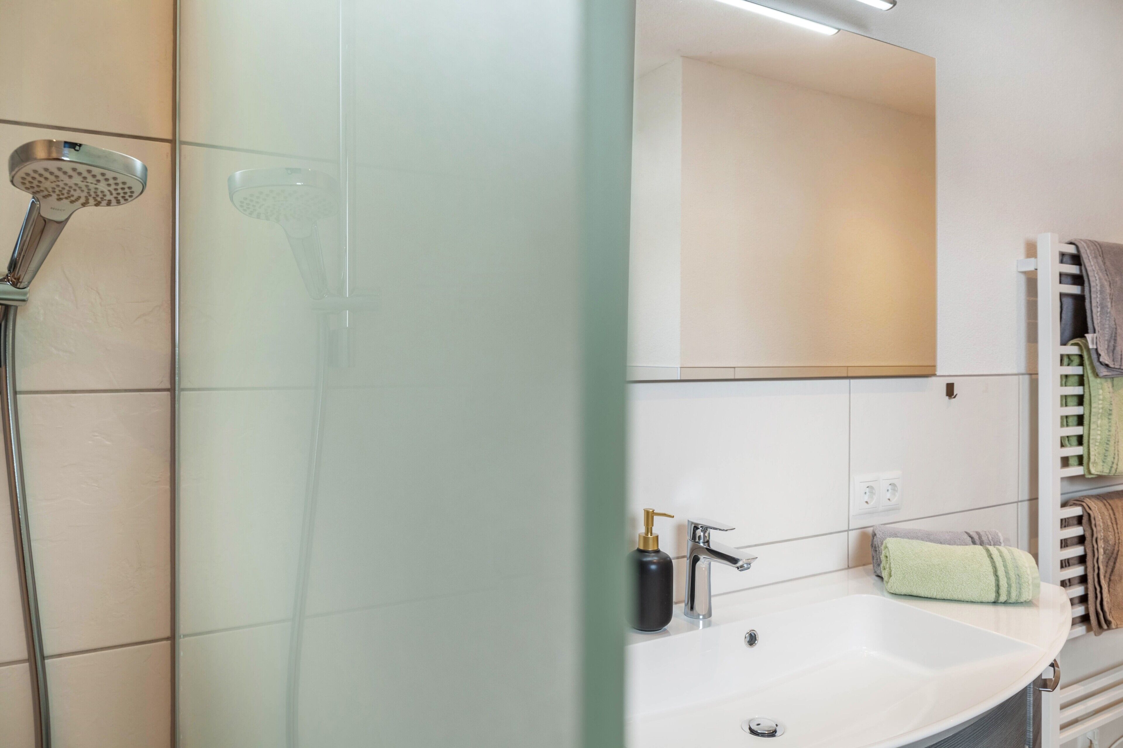 A modern bathroom with a shower, a sink, a mirror, and a towel rack.