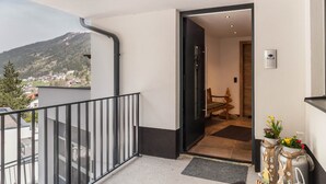 Ein Balkon mit Metallgeländer, eine Tür zu einem Raum mit Tisch und Stühlen sowie Blick auf einen Berg.