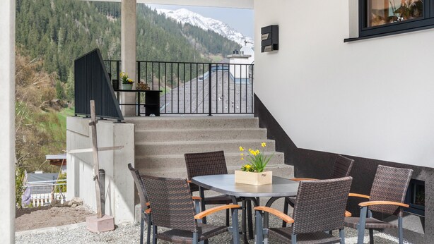 Ein Balkon mit Tisch und Stühlen, eine Treppe und Blick auf die Berge.