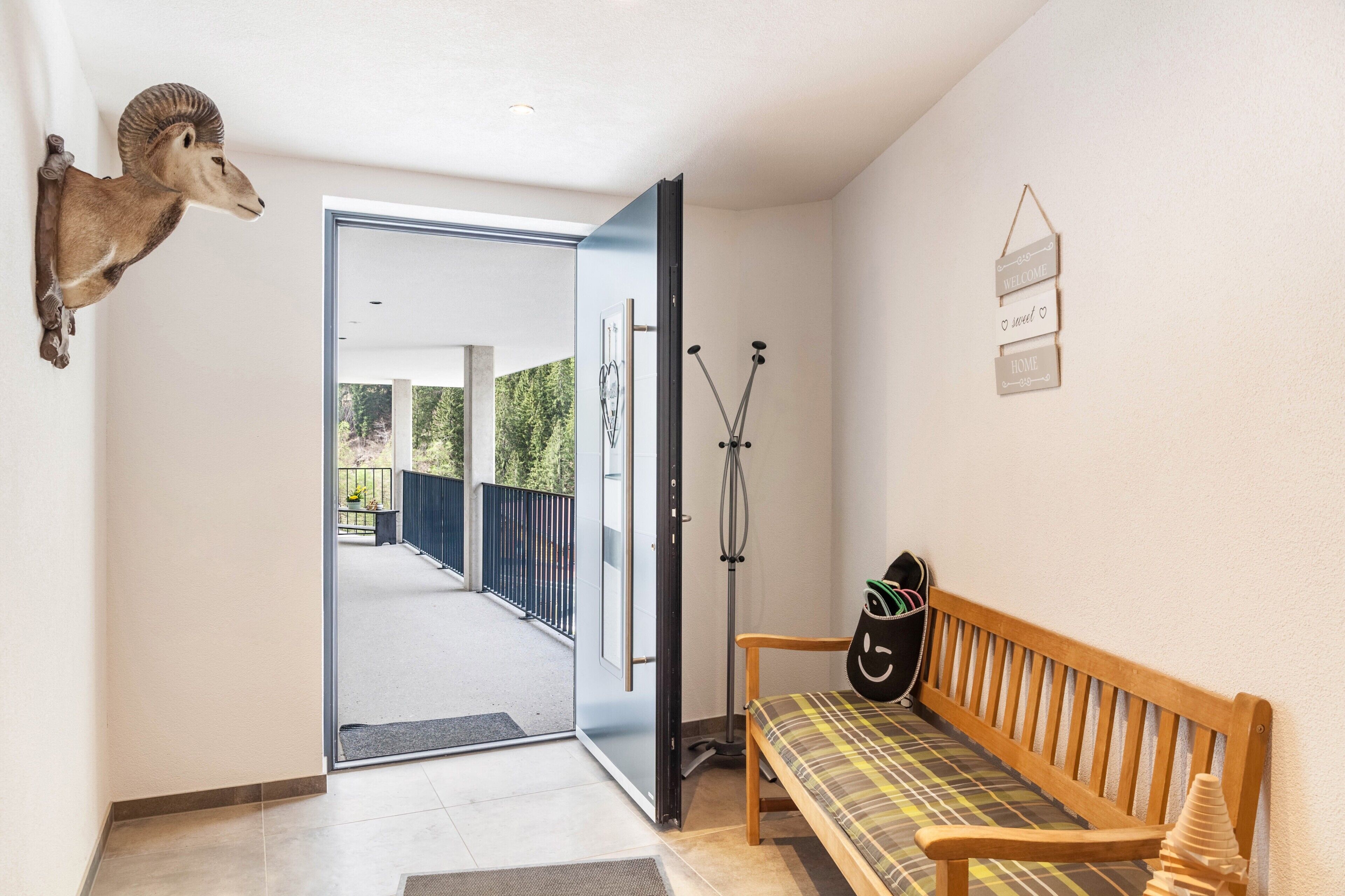 A hallway with a mounted animal head, a bench, a wall-mounted sign, and a door leading to an outdoor area.