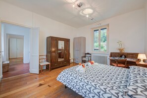 A bedroom with a bed, wooden wardrobe, a desk with a lamp, and a window with a view of greenery. - Mila Bike with wi-fi, Pollino di Premeno, Italy (Pollino di Premeno)