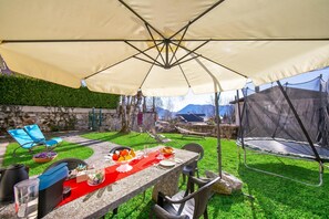 An outdoor patio with a table set for dining, surrounded by chairs and a large umbrella. - Mila Bike with wi-fi, Pollino di Premeno, Italy (Pollino di Premeno)