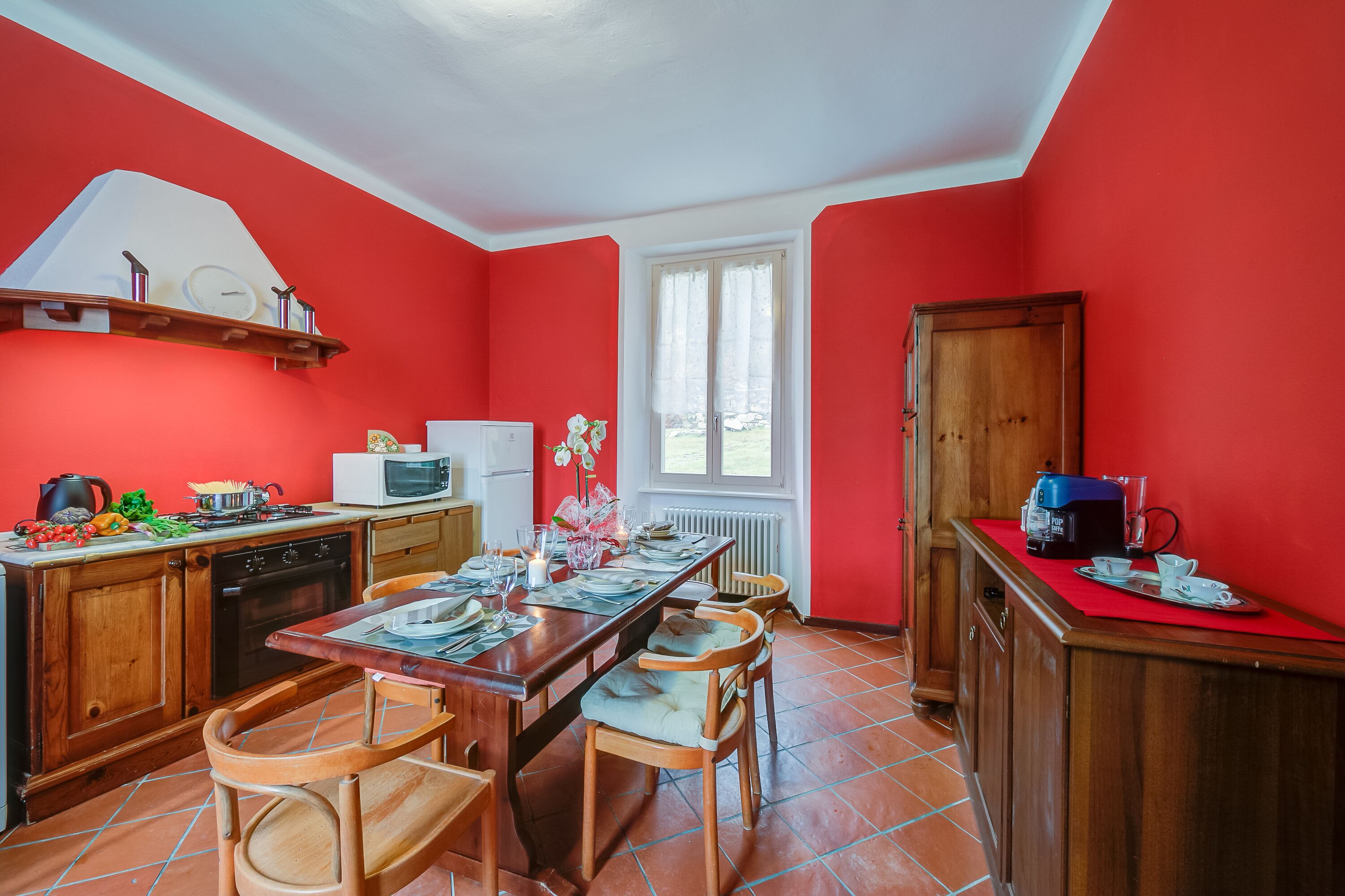 Una cocina con paredes rojas, armarios de madera, una mesa de comedor para cuatro personas y una cafetera sobre la encimera.