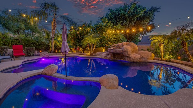 Una piscina con una formación rocosa, rodeada de palmeras y una silla roja.