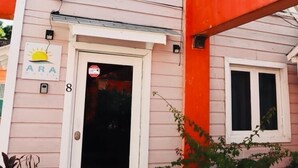 A pink building with a white door and windows, a small sign with a sun logo, and a number '8' on the door. - ARA OASIS - loft condo, 5 mins walk to beach (Negril)