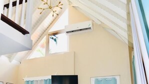 A spacious living area with a high ceiling, a staircase, a flat-screen TV, and a door with a curtain. - ARA OASIS - loft condo, 5 mins walk to beach (Negril)