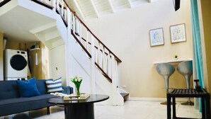 A modern living room with a staircase, a sofa, a coffee table, and a washing machine. - ARA OASIS - loft condo, 5 mins walk to beach (Negril)