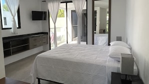 Une chambre moderne avec un grand lit, un téléviseur fixé au mur et une vue sur l’extérieur par les fenêtres.