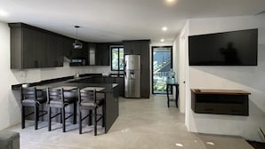 Une cuisine moderne avec des meubles de couleur sombre, un îlot central doté de sièges, un réfrigérateur encastré et une grande fenêtre.
