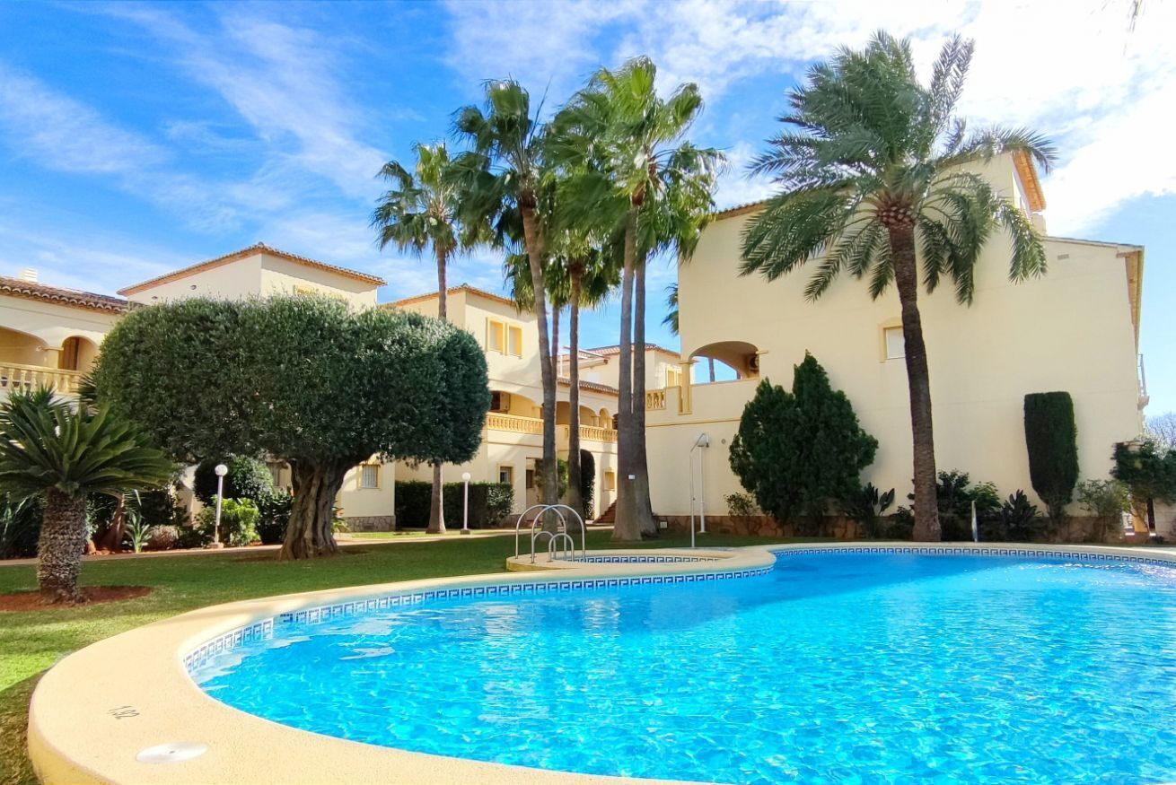 A swimming pool surrounded by palm trees and a building with a tiled roof.