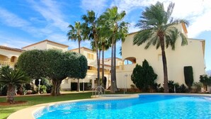 A swimming pool surrounded by palm trees and a building with a tiled roof.