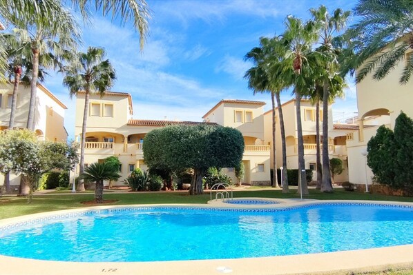 A swimming pool surrounded by palm trees and a building with balconies.