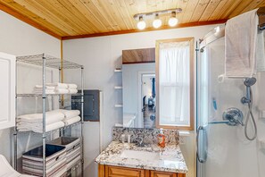 Compact bathroom with shelf, sink, and glass-enclosed shower.