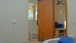 A hotel room with a bed, a wooden door, a bench, a small table, and a view of the outside. - Lufesa Apartments (Mogan)