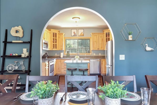 Una cocina con armarios de madera, una isla central y una zona de comedor con mesa y sillas.