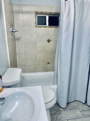 A bathroom with a toilet, sink, bathtub, and a window. - The Doze Off (Houston)