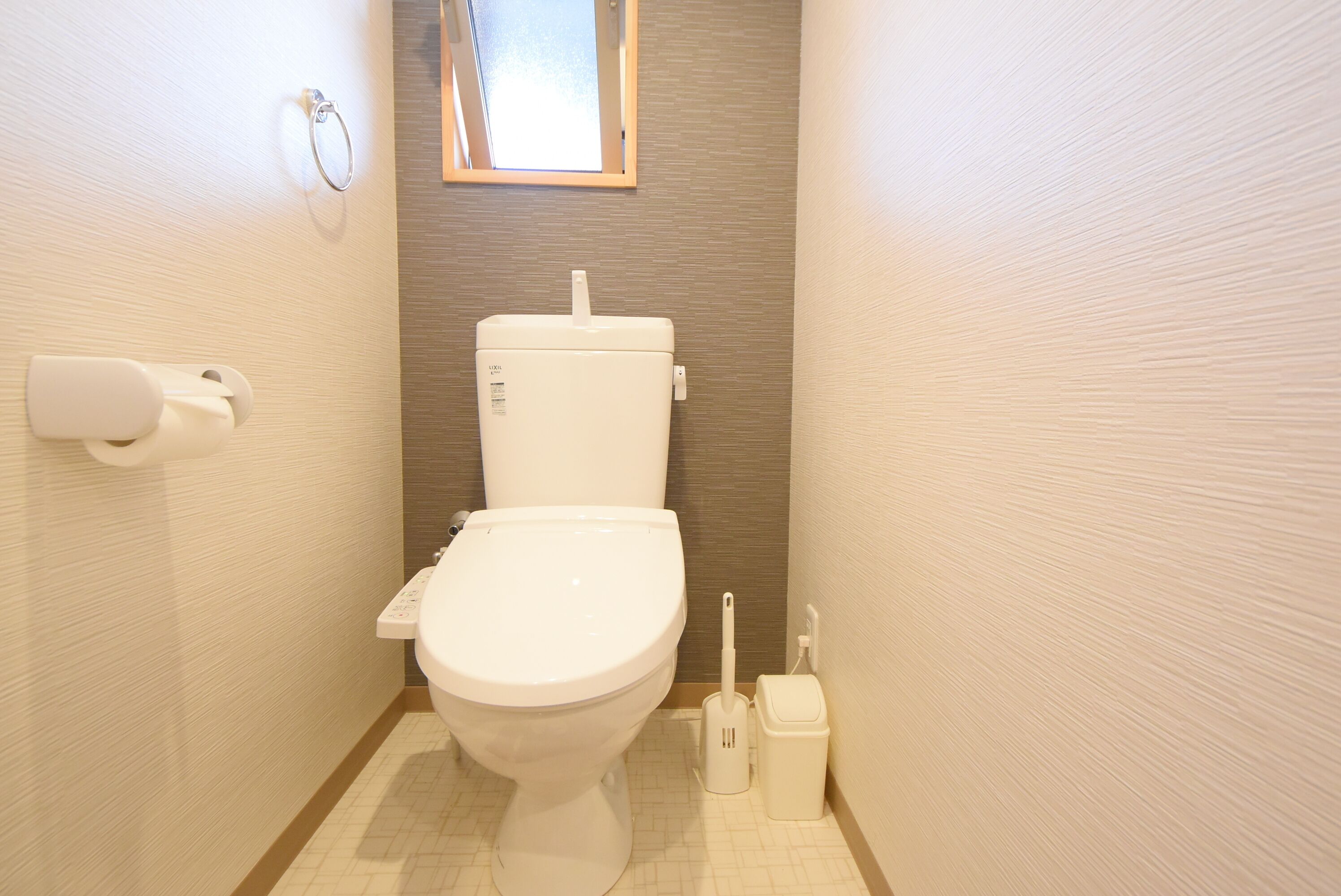 A small, modern bathroom with a toilet, toilet paper holder, bidet, and a window above the toilet.