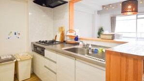 Cocina moderna con un lavaplatos de acero inoxidable, estufa a gas y encimera de madera. Se observan dos cubos de basura y una ventana con cortinas.