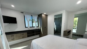 Un dormitorio moderno con una cama grande, un armario empotrado, un televisor montado en la pared y una zona de ducha visible a través de una puerta de vidrio.