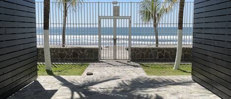 A view from a covered patio to a beach, with a stone wall and palm trees.