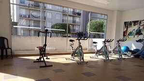 Une salle de sport équipée de vélos d’appartement, d’un banc et d’une grande fenêtre donnant sur un quartier résidentiel.