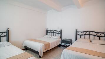 Habitación de hotel con tres camas, cada una con cabecera y mesita de noche.