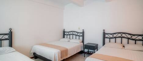 Habitación de hotel con tres camas, cada una con cabecera y mesita de noche.