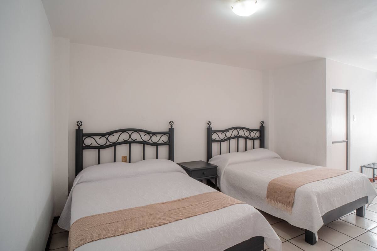 Two single beds with black metal headboards, white bedding, and a small bedside table with a lamp.