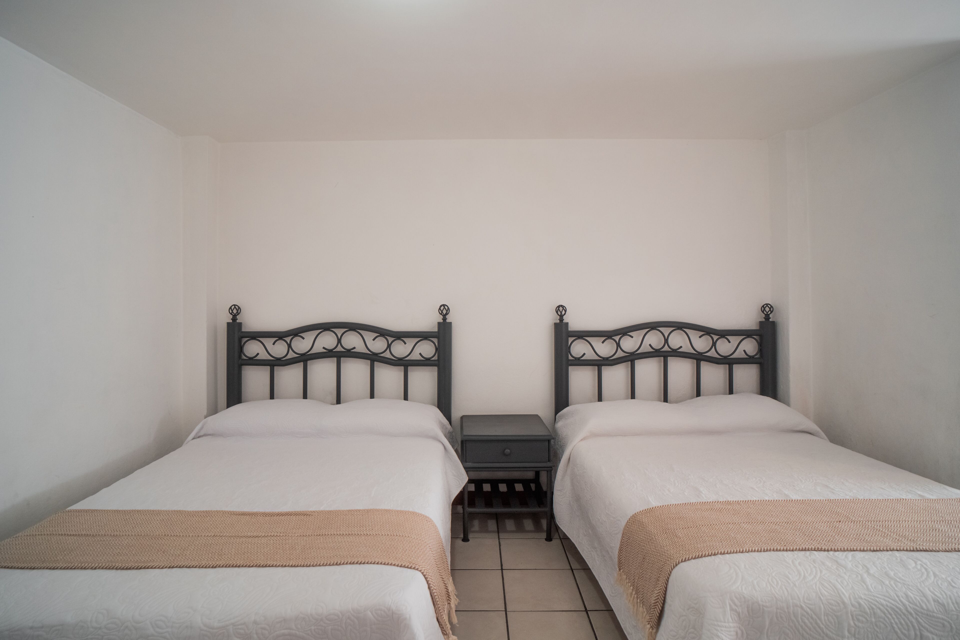 Une chambre double avec deux lits, une table de chevet et un sol carrelé.