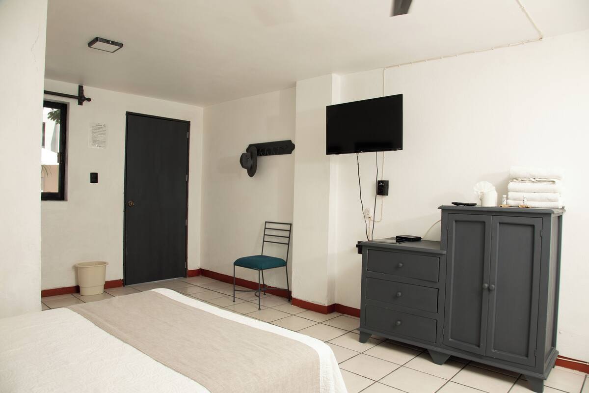 A bedroom with a bed, a chair, a wardrobe, a television, and a door.