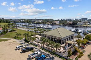 A marina with boats docked, a building with a green roof, and a parking area with cars.