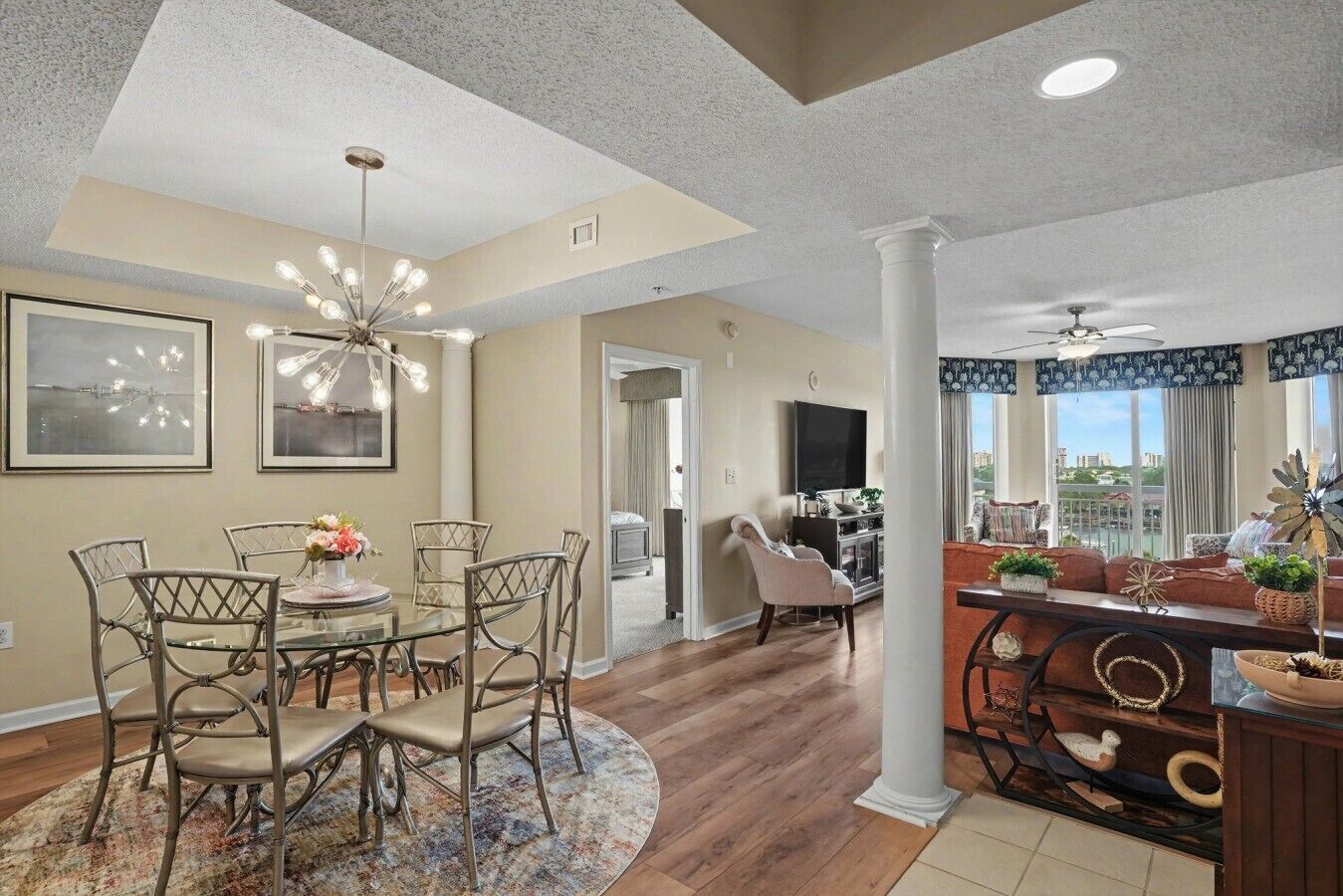 A spacious living room with a dining area, a large window with a view, and a modern chandelier.