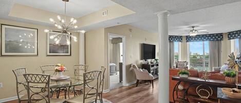 A spacious living room with a dining area, a large window with a view, and a modern chandelier.