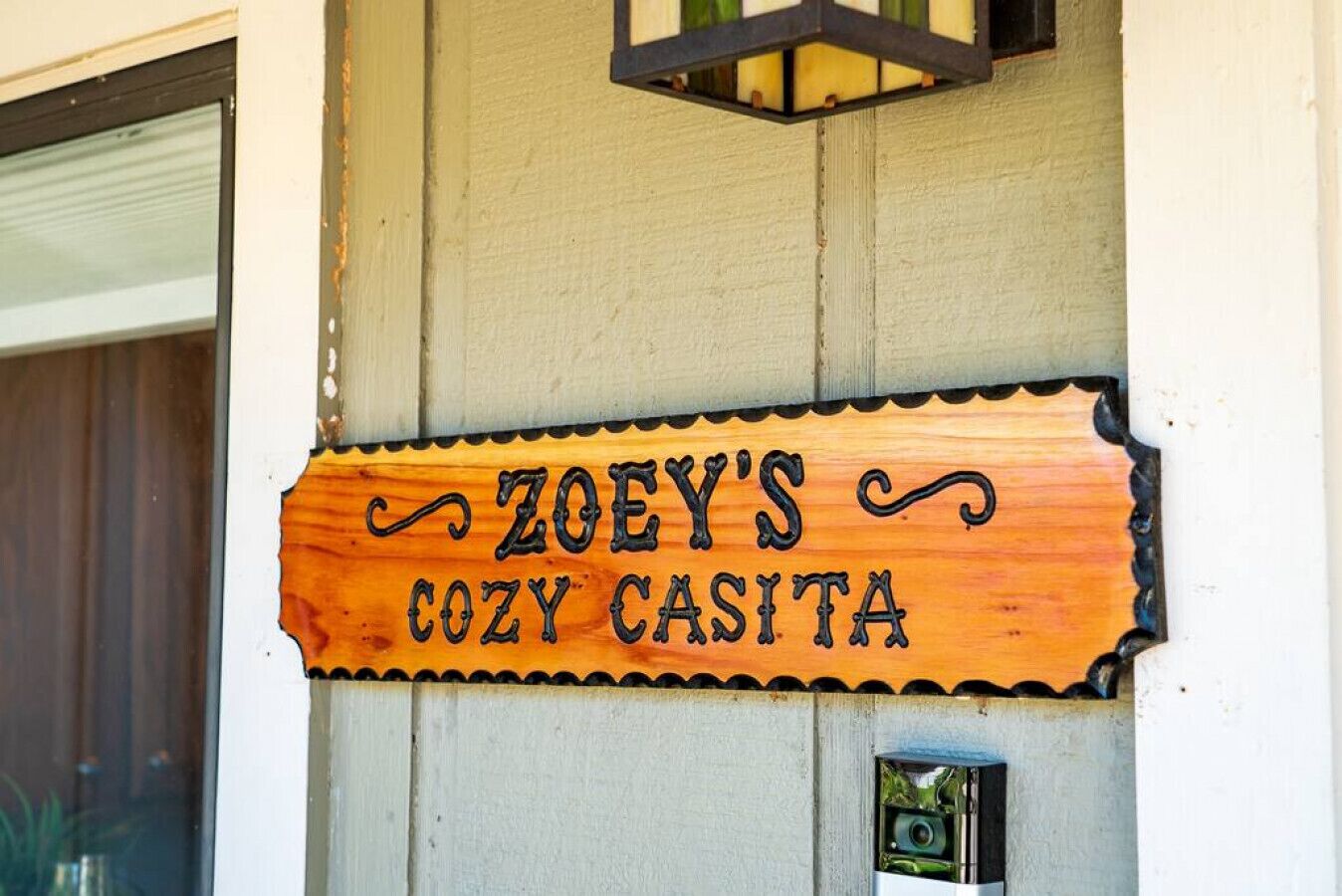 Een houten bord met de tekst 'ZOEY'S COZY CASITA' aan een muur bevestigd.