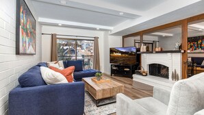 A modern living room with a blue sofa, a wooden coffee table, and a fireplace. - Park Station 133 2 Bedroom Condo by RedAwning (Park City)