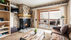 Una sala de estar acogedora con chimenea de piedra, una mesa de centro de madera, un sofá y una estantería.