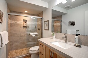 A modern bathroom with a glass-enclosed shower, a sink with a mirror, and wooden cabinets.