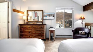 Quarto com duas camas, penteadeira de madeira, espelho, televisão, janela com vista para uma paisagem nevada e luminária.