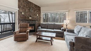 A cozy living room with a stone fireplace, a gray sofa, a recliner, and a coffee table. - Snow Flower 130 2 Bedroom Condo by RedAwning (Park City)