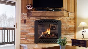 A fireplace with a stone surround, a television above it, and a potted plant on a wooden table in front. - Snow Flower 122 2 Bedroom Condo by RedAwning (Park City)