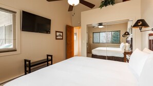 A bedroom with a large bed, a ceiling fan, a TV, and a bedside table with a lamp. - Snow Flower 122 2 Bedroom Condo by RedAwning (Park City)