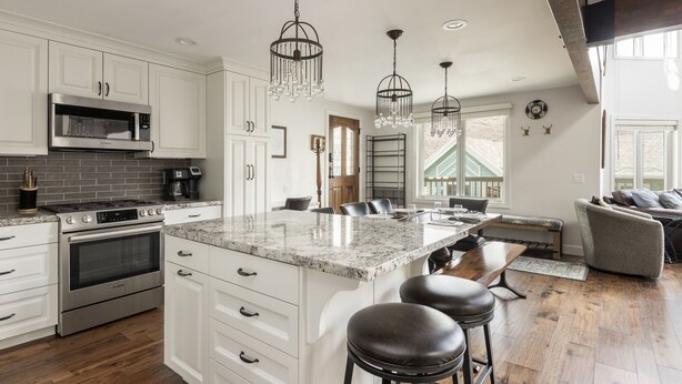 A spacious kitchen with white cabinetry, a large island with bar stools, stainless steel appliances, and pendant lighting.