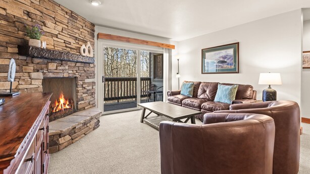 A living room with a stone fireplace, leather furniture, and a view through a glass door. - Snow Flower 149 2 Bedroom Condo by RedAwning (Park City)